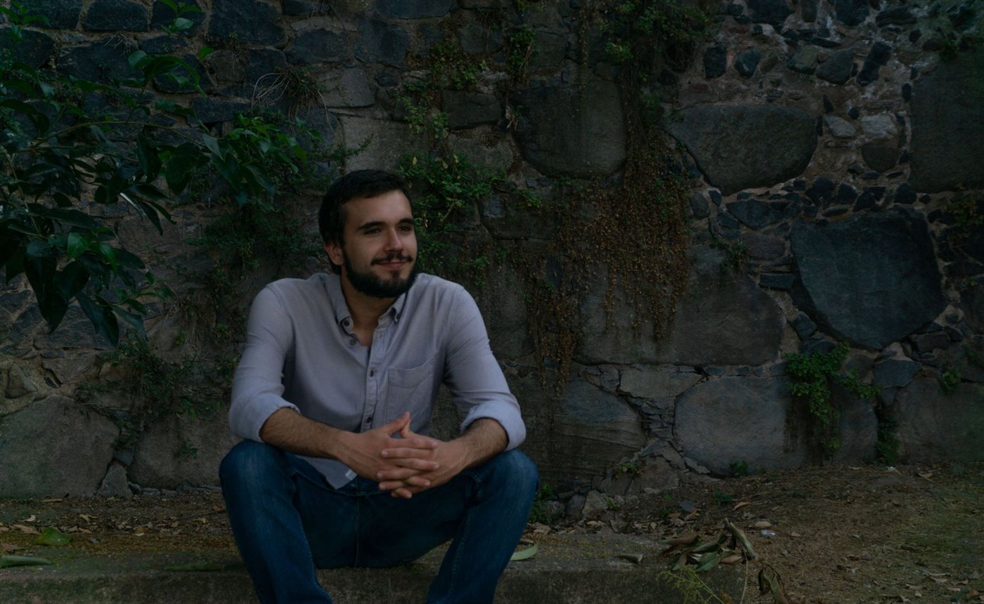 Vasco, host of Beyond Tejo, sitting by an old stone wall